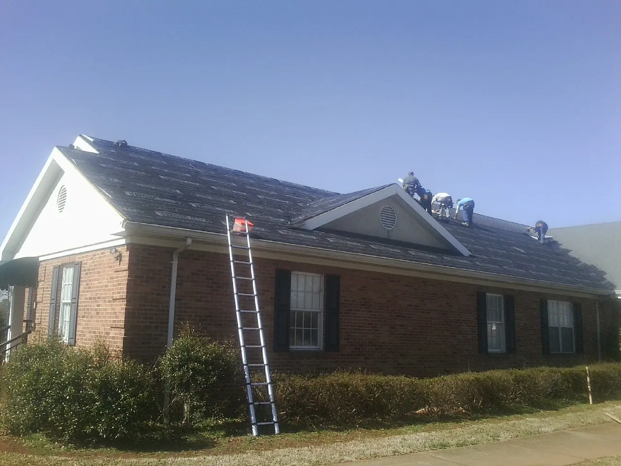Crew tearing shingles off a brick ranch roof with a ladder set — Emergency Roof Repair work by our crew in Turners Falls