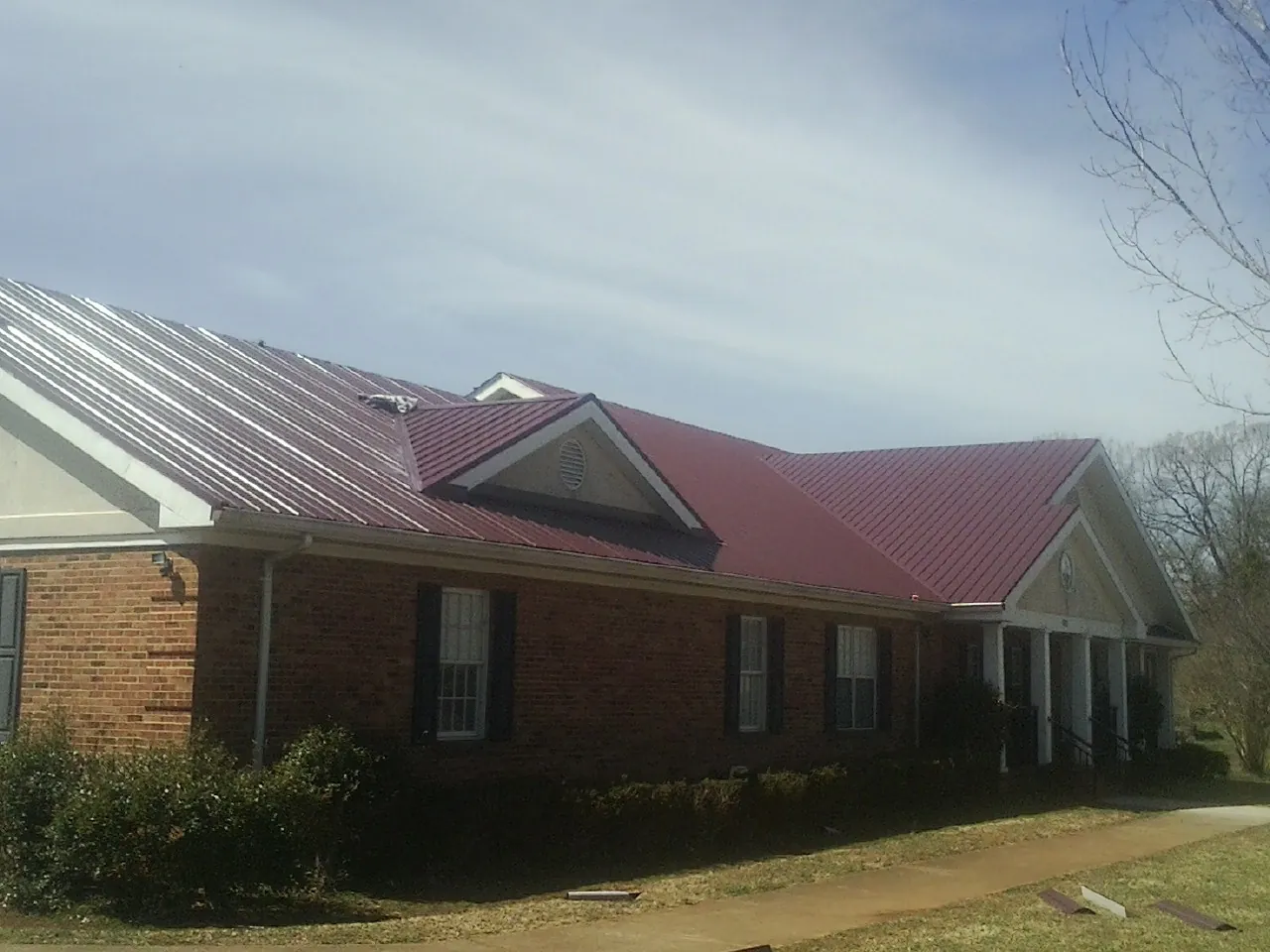 Red metal roof with gabled entries on a long brick building, from a Hail Damage Roof Repair job in Turners Falls