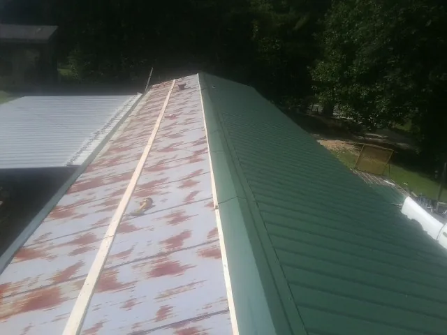 Old rusted panels beside newly installed green metal roofing — Wind Damage Roof Repair by Roofing Brothers in Turners Falls