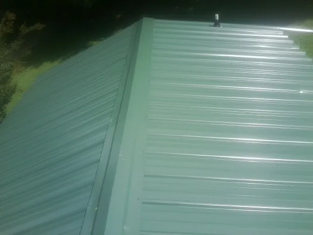 New green metal panels meeting at the ridge of a roof — Flat Roof Repair work by our crew in Turners Falls