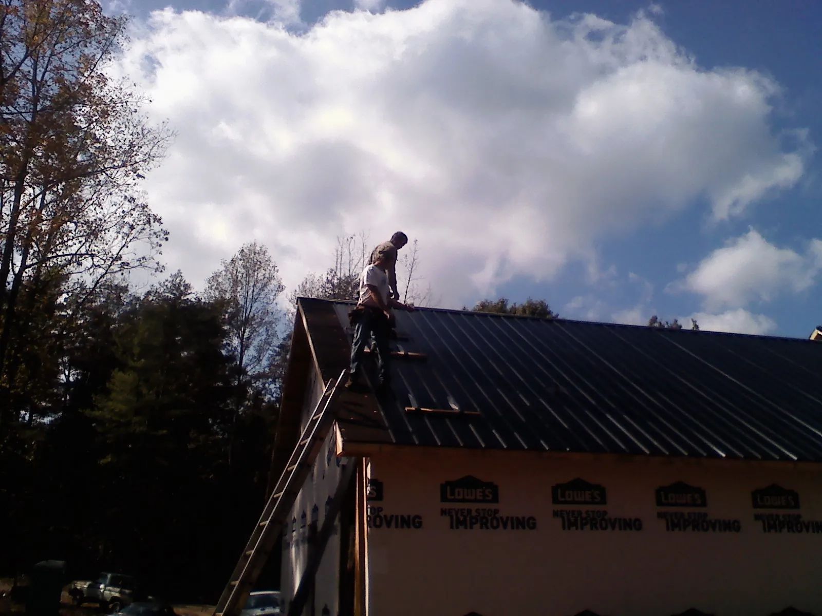 Roofer fastening dark metal panels high against a cloudy sky, from a Roof Inspection job in Turners Falls