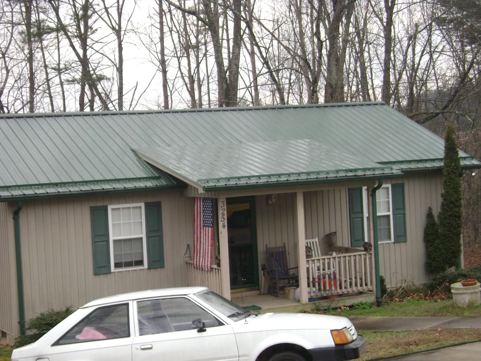 Green metal roof and front porch on a tan sided cottage in Turners Falls