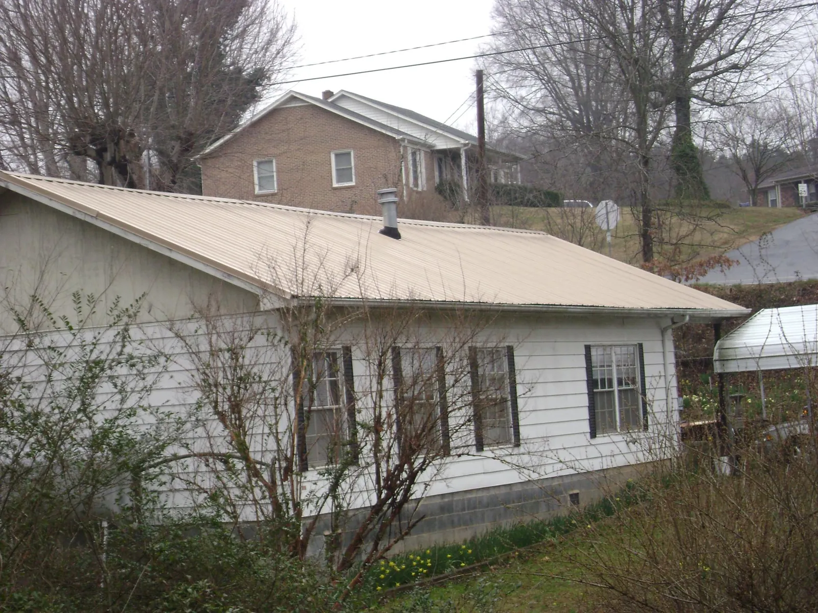 Tan metal roof on a white sided house set into a hillside — Commercial Roofing by Roofing Brothers in Turners Falls