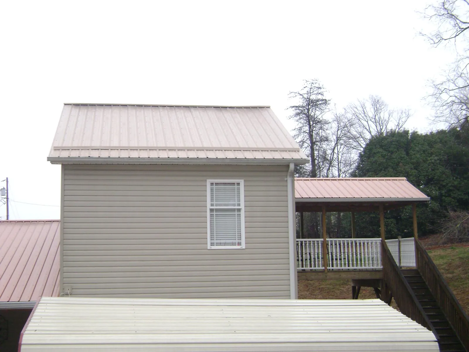 Tan metal roofs on a two story addition and attached porch, from a Roof Replacement job in Turners Falls